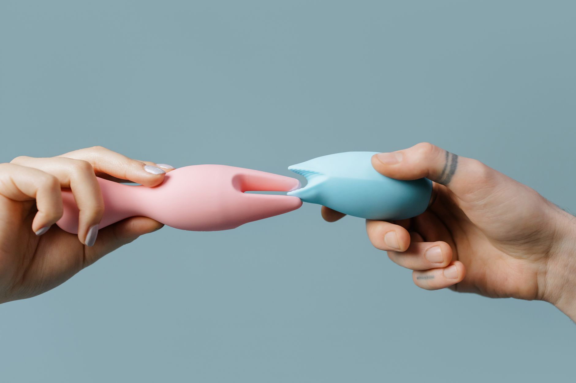 Hands holding pastel-colored silicone sex toys on a soft background