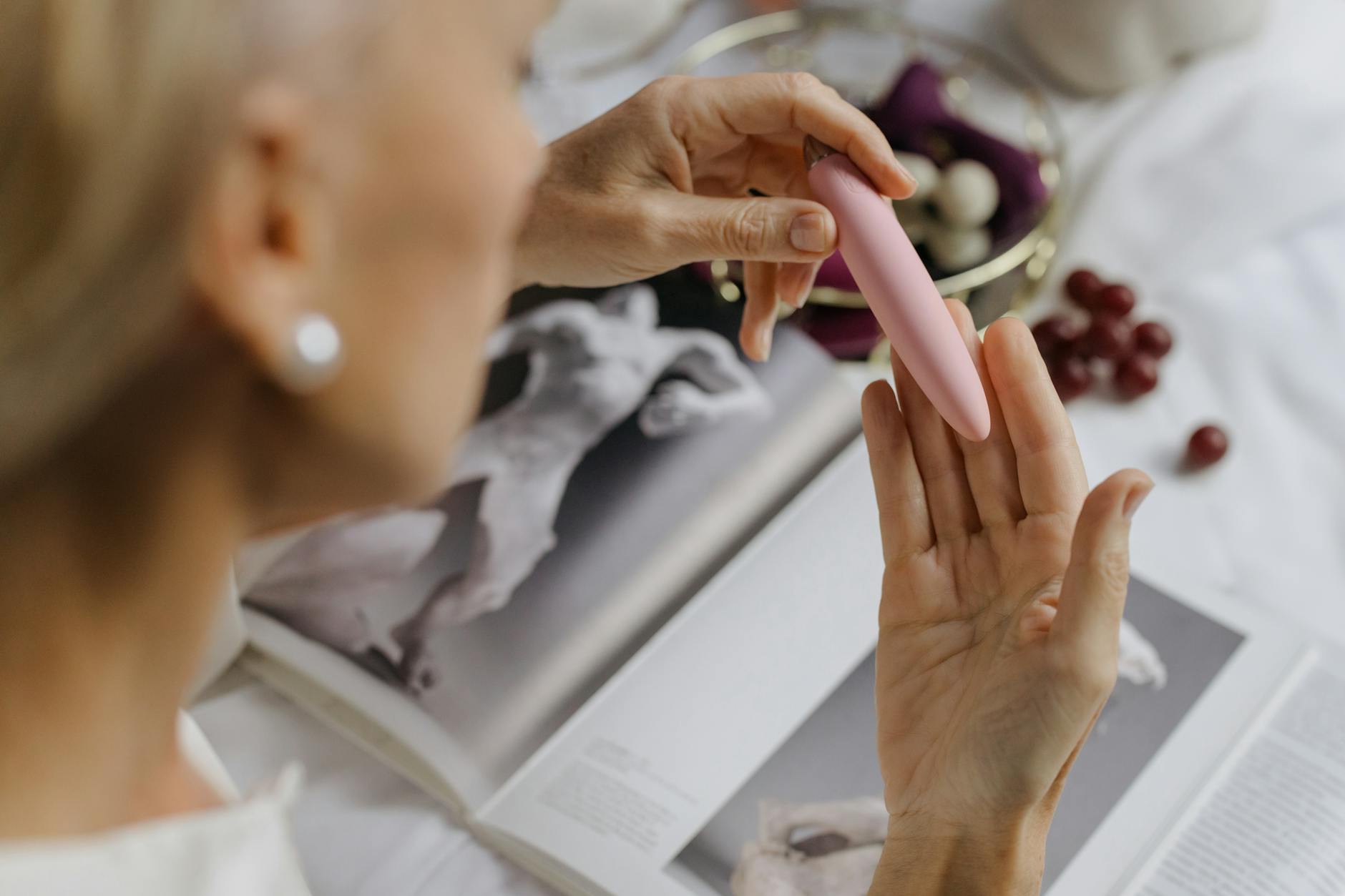 Woman holding a pink vibrator with art books nearby, symbolizing personal pleasure and intimate choice