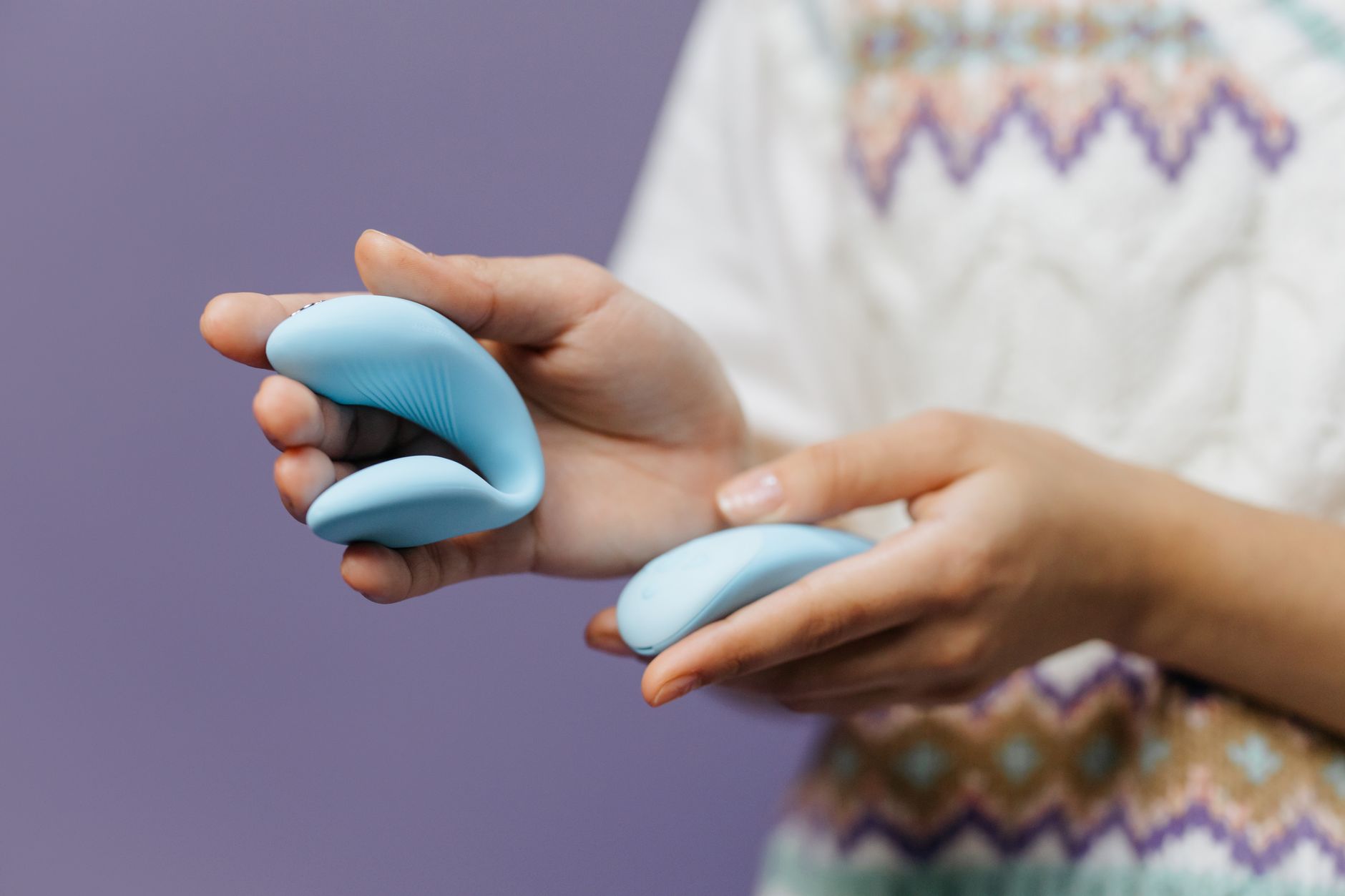 Hands holding a sleek blue clitoral vibrator against a purple background, showcasing intimate self-pleasure.