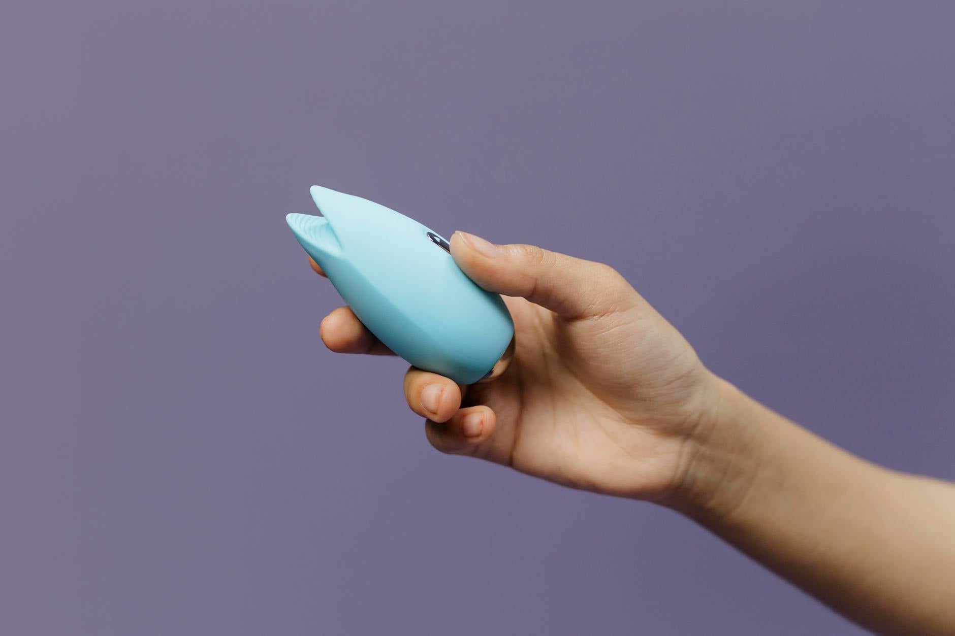 Hands holding a sleek blue vibrator against a purple background, demonstrating discreet adult toy use