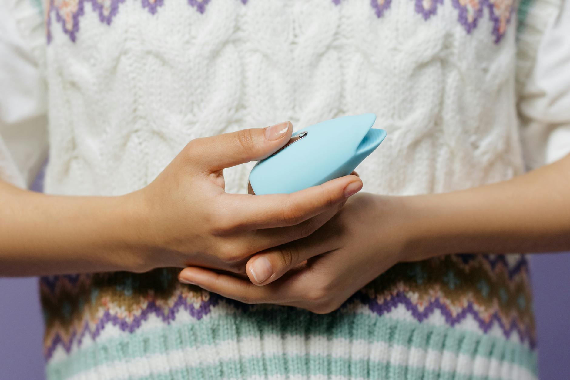 Close-up of hands holding a blue lemon vibrator against a knitted sweater.