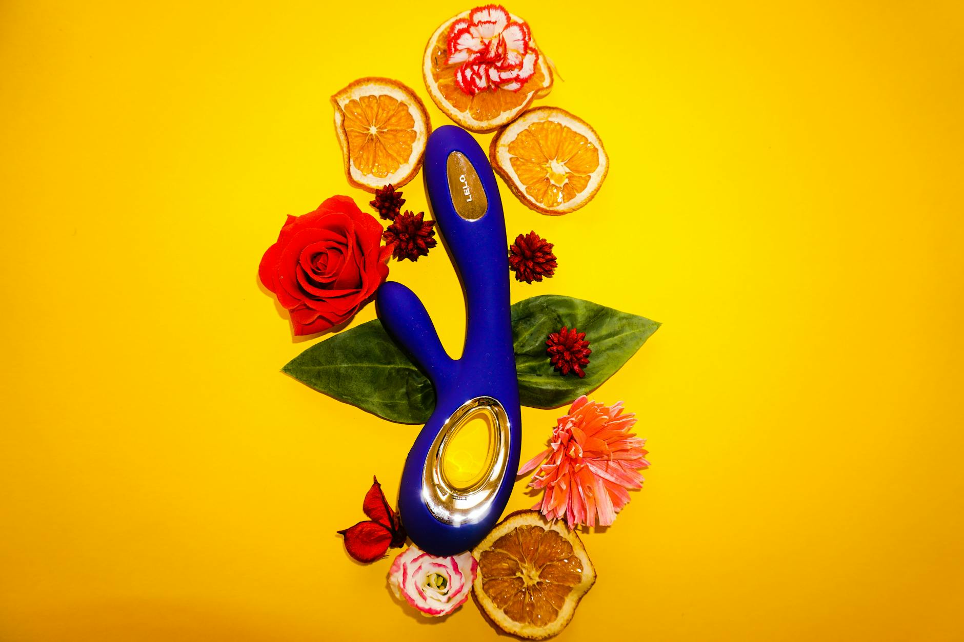 A blue lemon clitoral vibrator surrounded by flowers and citrus on a bright yellow background.