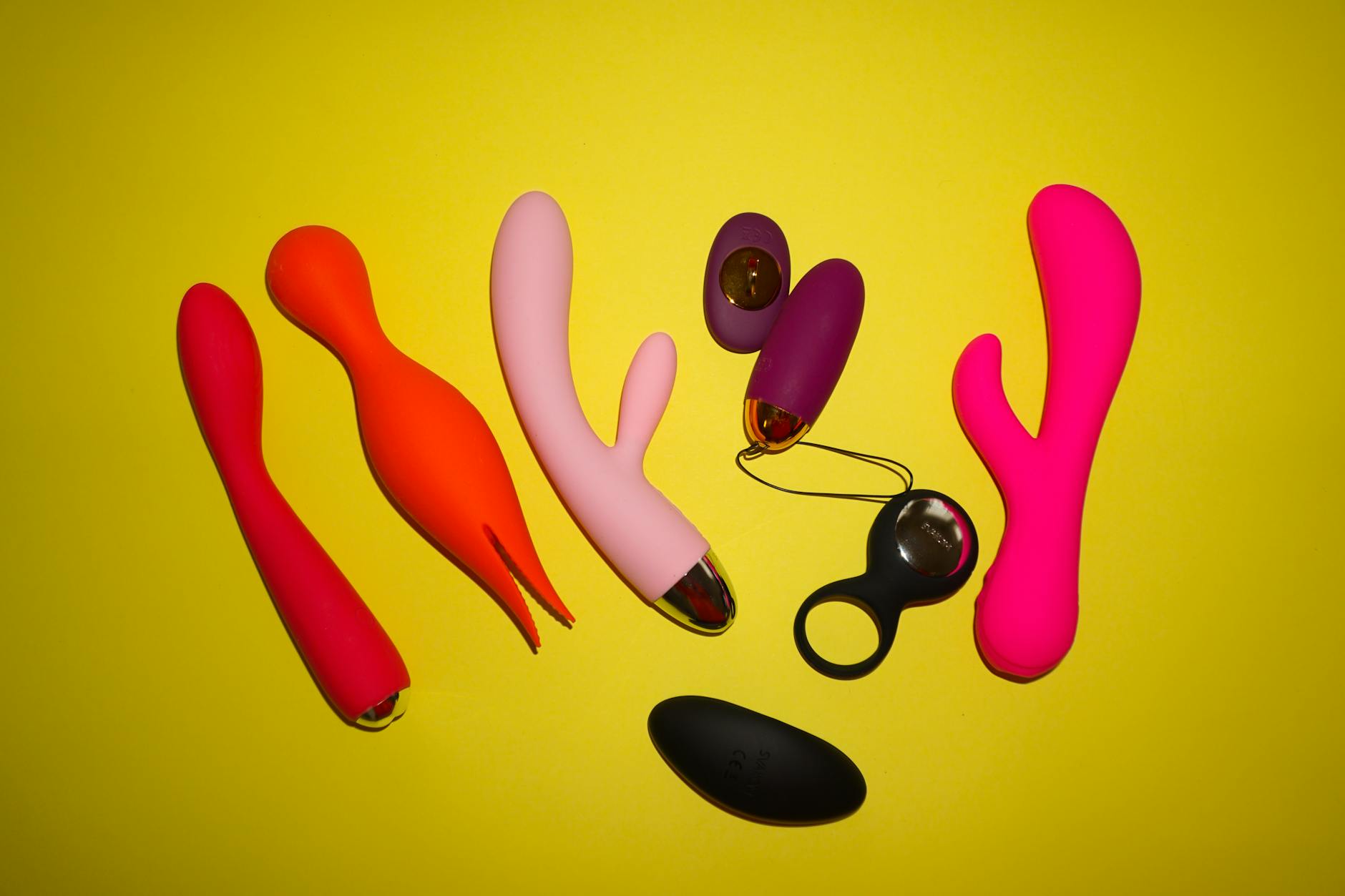 Colorful clitoral vibrators and sex toys on a bright yellow background, showcasing various pleasure tools